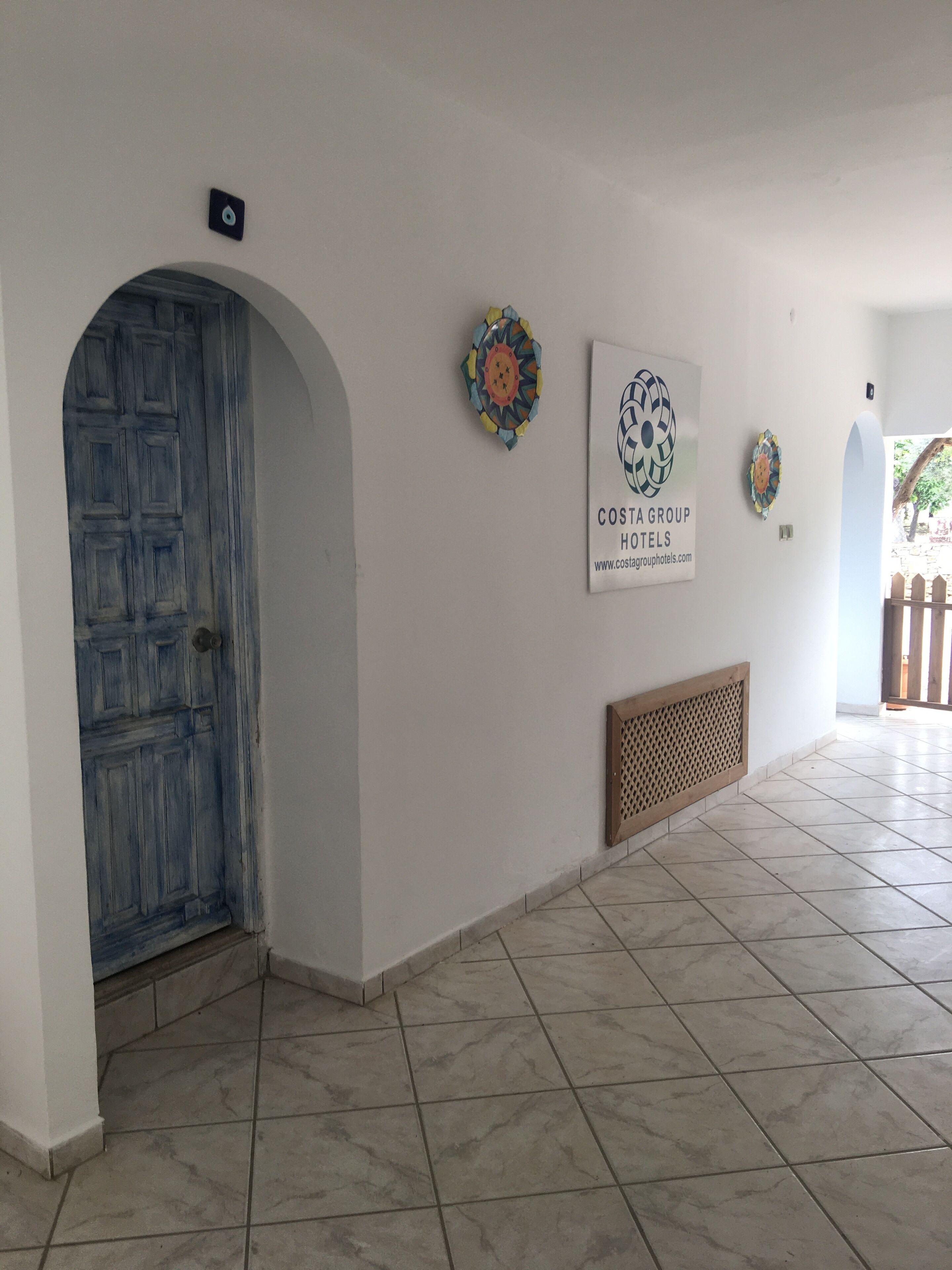 A hallway with a blue door, tiled floor, and decorative wall art.