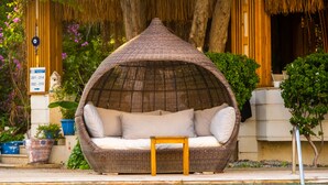 A poolside seating area with a thatched roof, a small table, and a wicker sofa with cushions. - Costa Bodrum City (Bodrum)