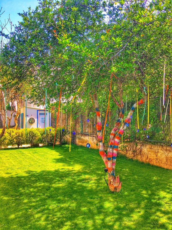A garden with a tree decorated with colorful ribbons and blue ornaments.