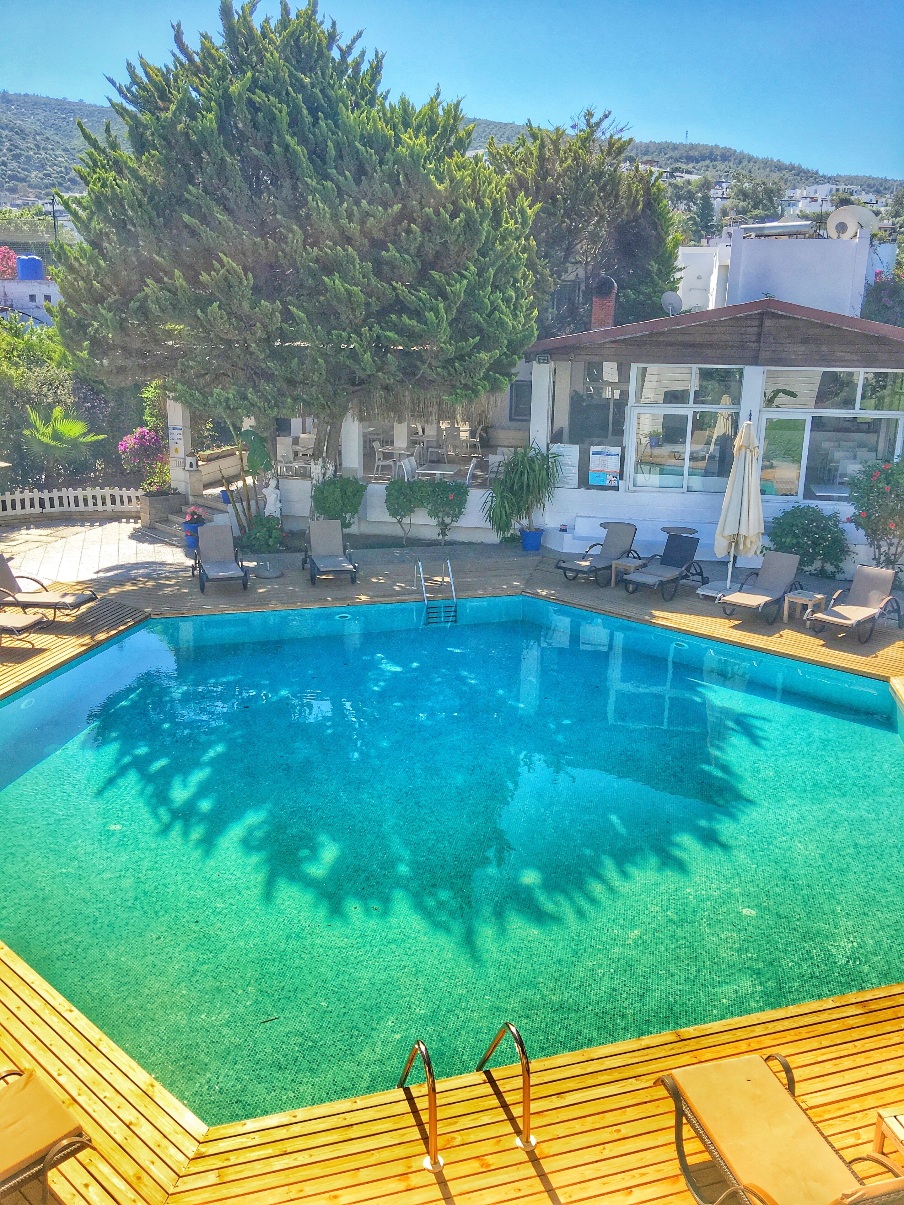 Una piscina azul cristalina rodeada de sillones de relax y una terraza de madera.