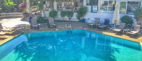 Una piscina azul cristalina rodeada de sillones de relax y una terraza de madera.