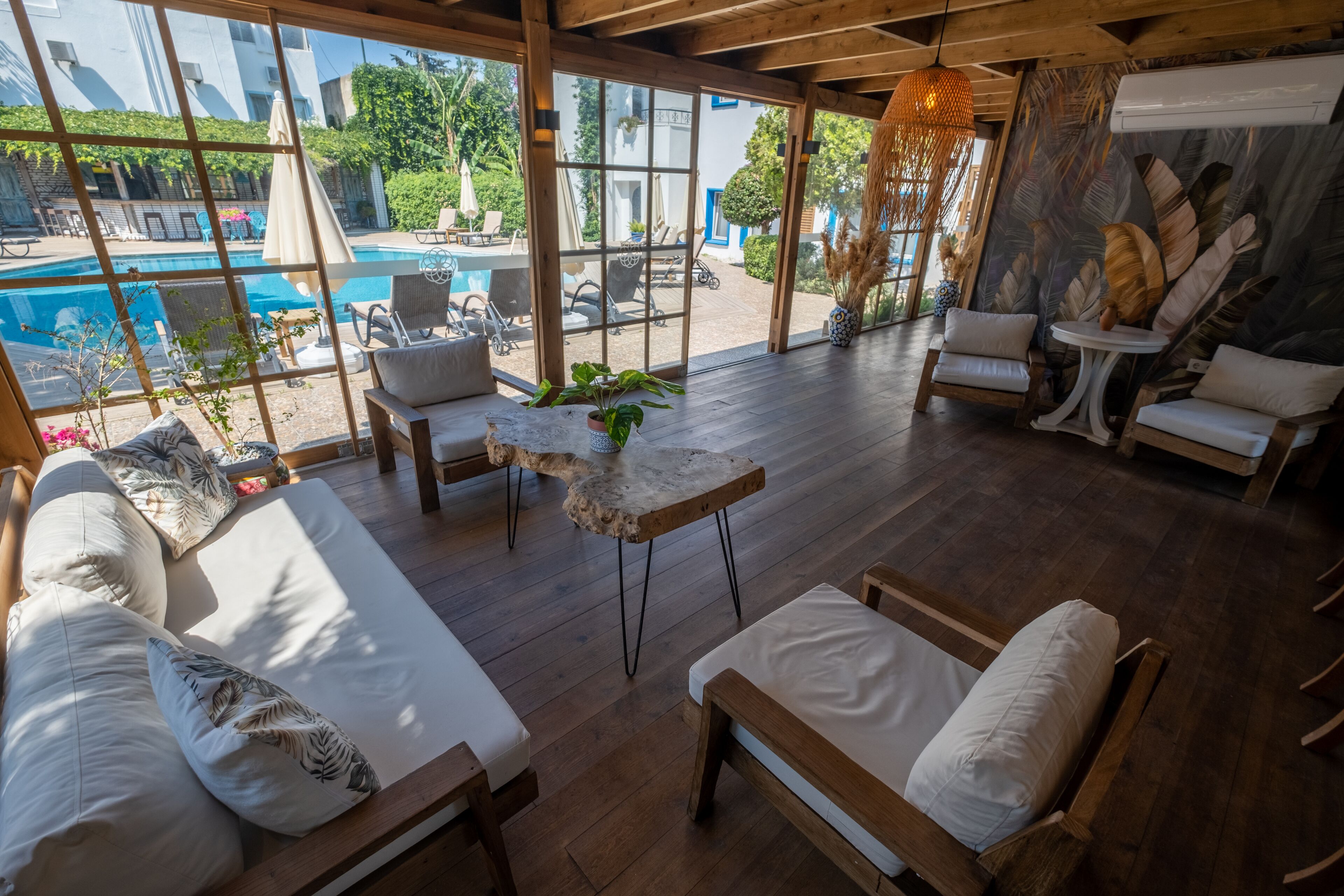 Un vaste espace extérieur aménagé avec un sol en bois, des canapés blancs confortables et une vue sur une piscine.