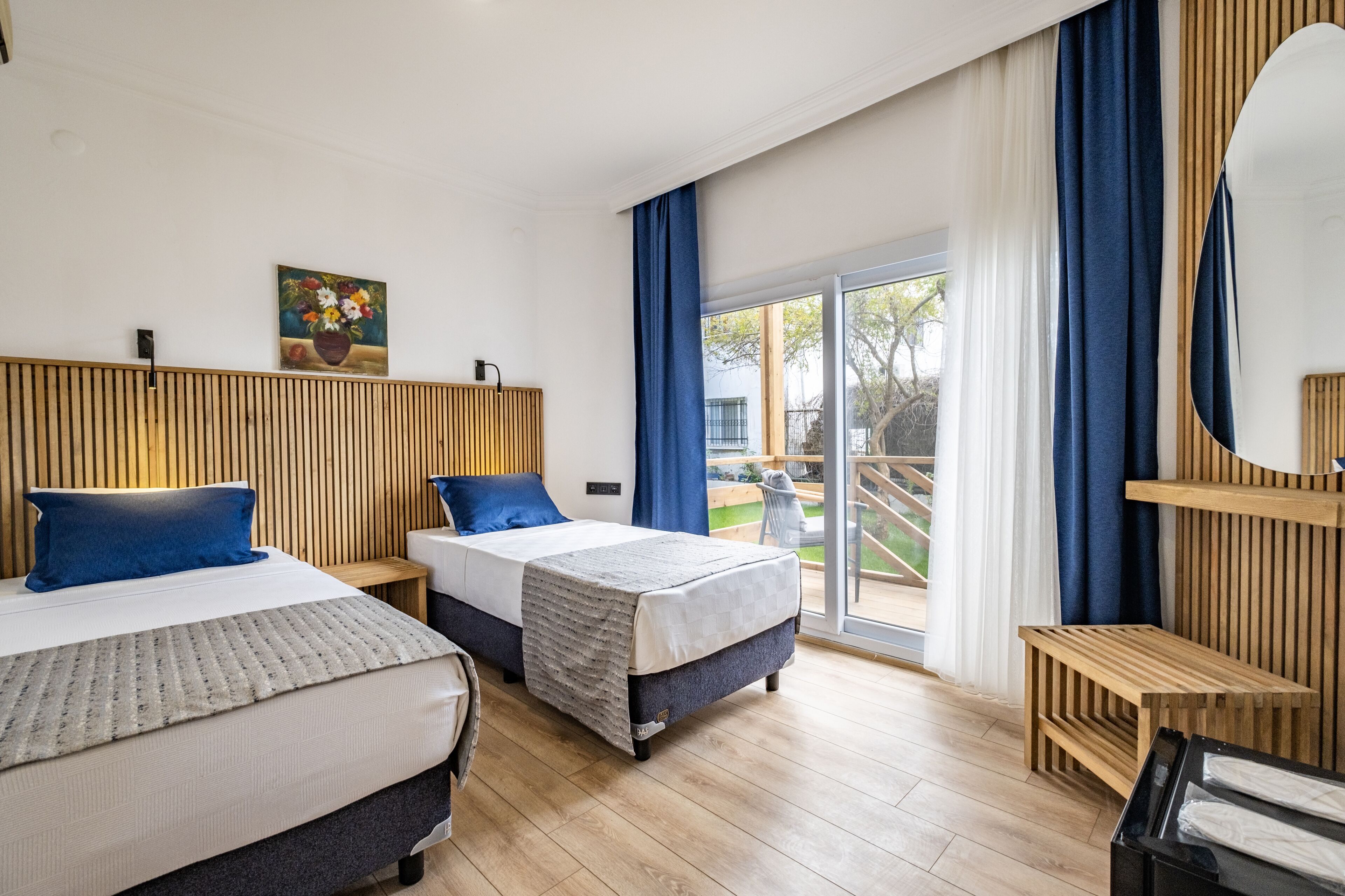 Une chambre d’hôtel moderne avec deux lits, une tête de lit en bois, une grande fenêtre avec des rideaux et une vue sur l’extérieur.