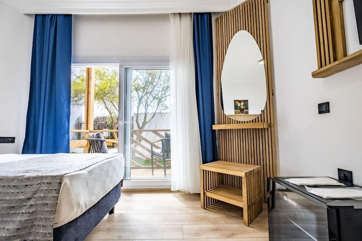 Ein Hotelzimmer mit einem Bett, einer Holzbank, einem Spiegel und Blick ins Freie.
