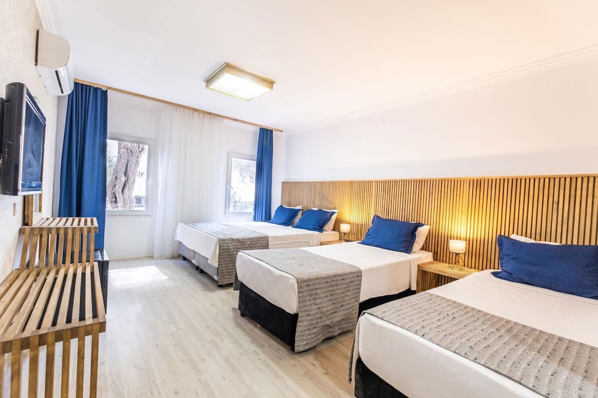 A hotel room with two beds, a TV, a wooden bench, and a window with curtains.
