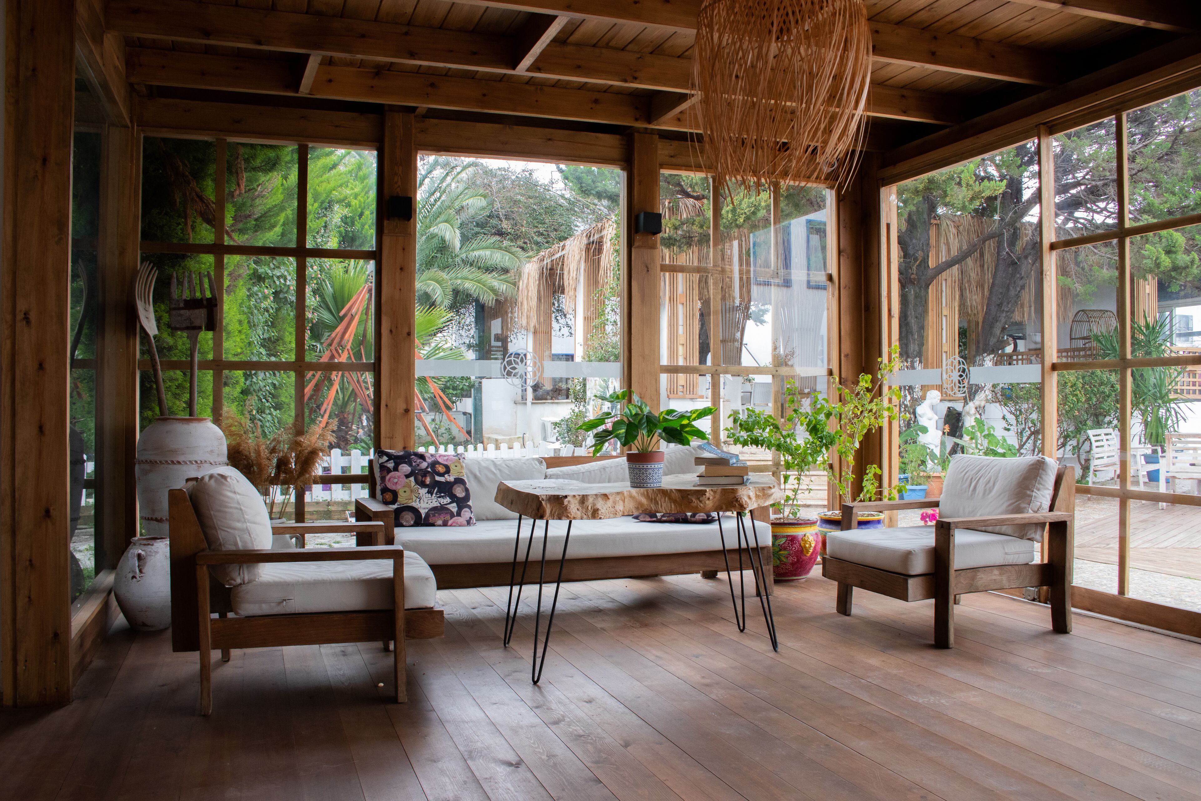 A wooden deck with a sofa and chairs, large windows, and potted plants.