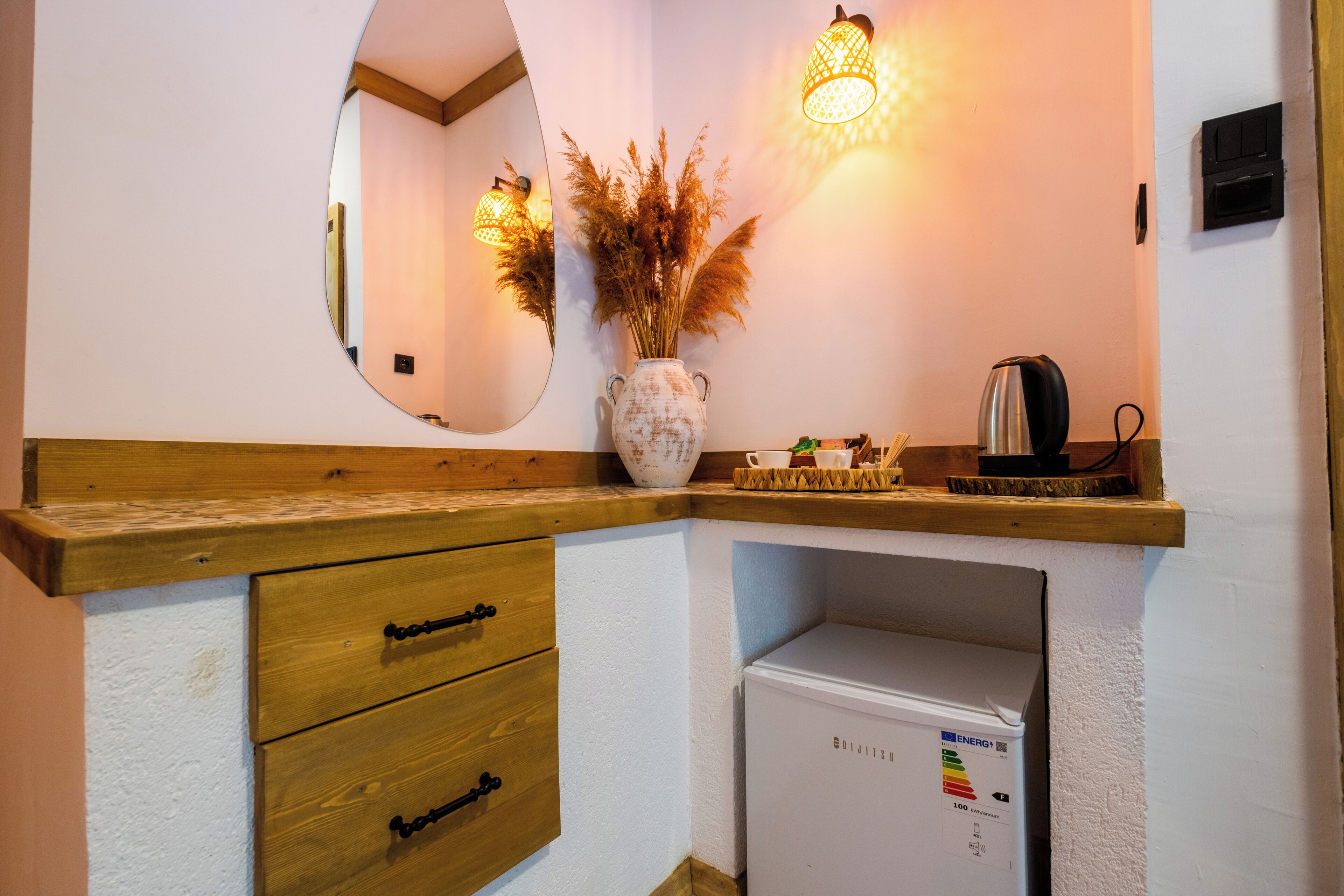 Una cocina con armarios de madera, un refrigerador blanco, un espejo y un jarrón con plantas secas.