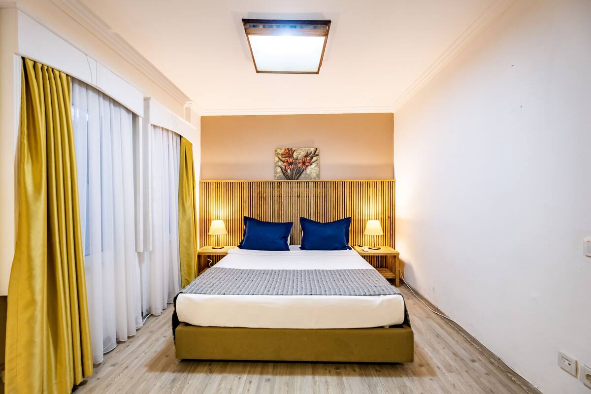 A hotel room with a large bed, two bedside tables with lamps, a ceiling light, and a wall-mounted artwork.
