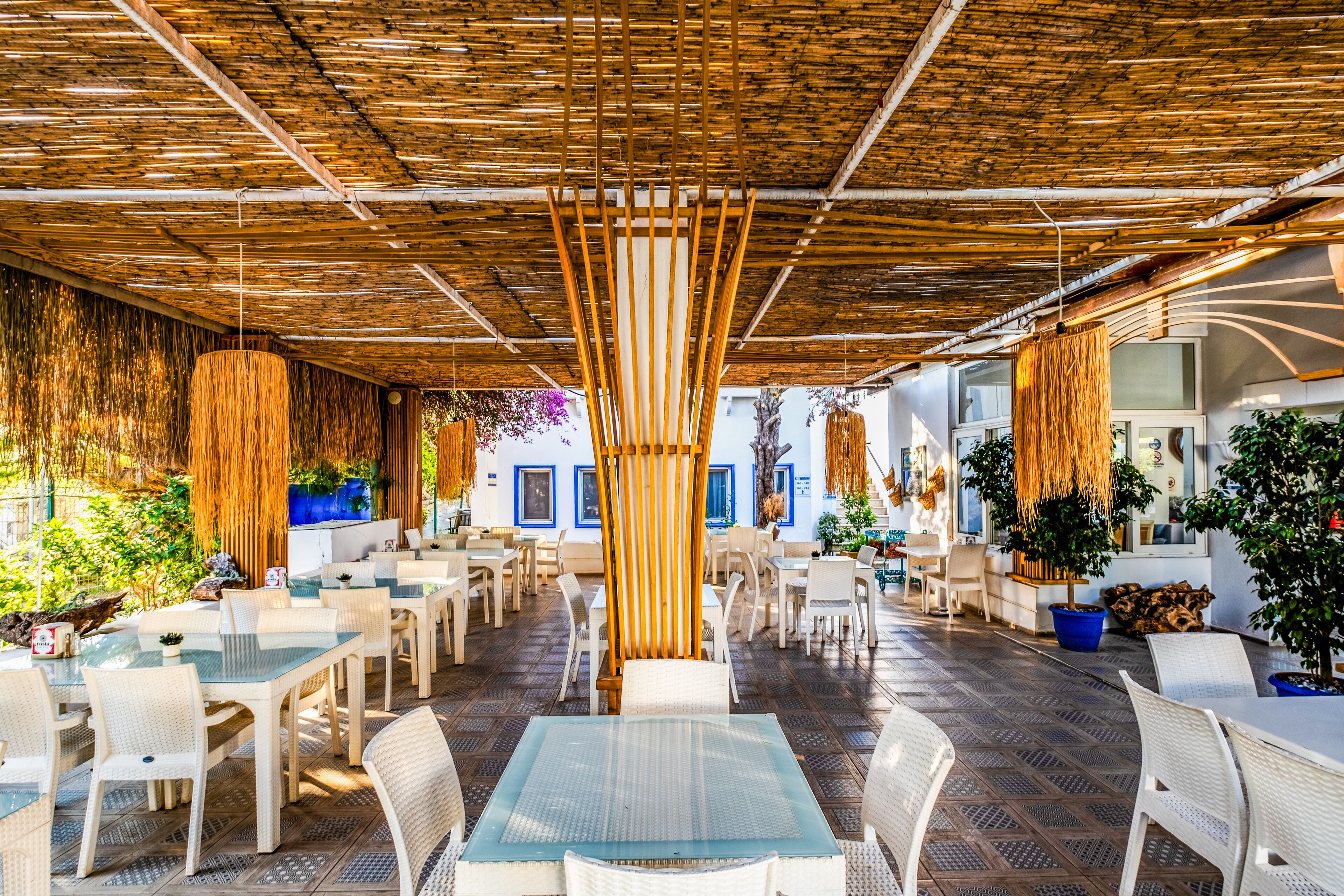 An outdoor café with white wicker furniture, a thatched roof, and potted plants.