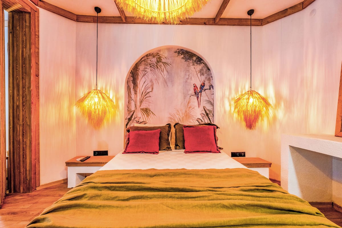 A bedroom with a large bed, two nightstands, a wooden door, and a mural on the wall.