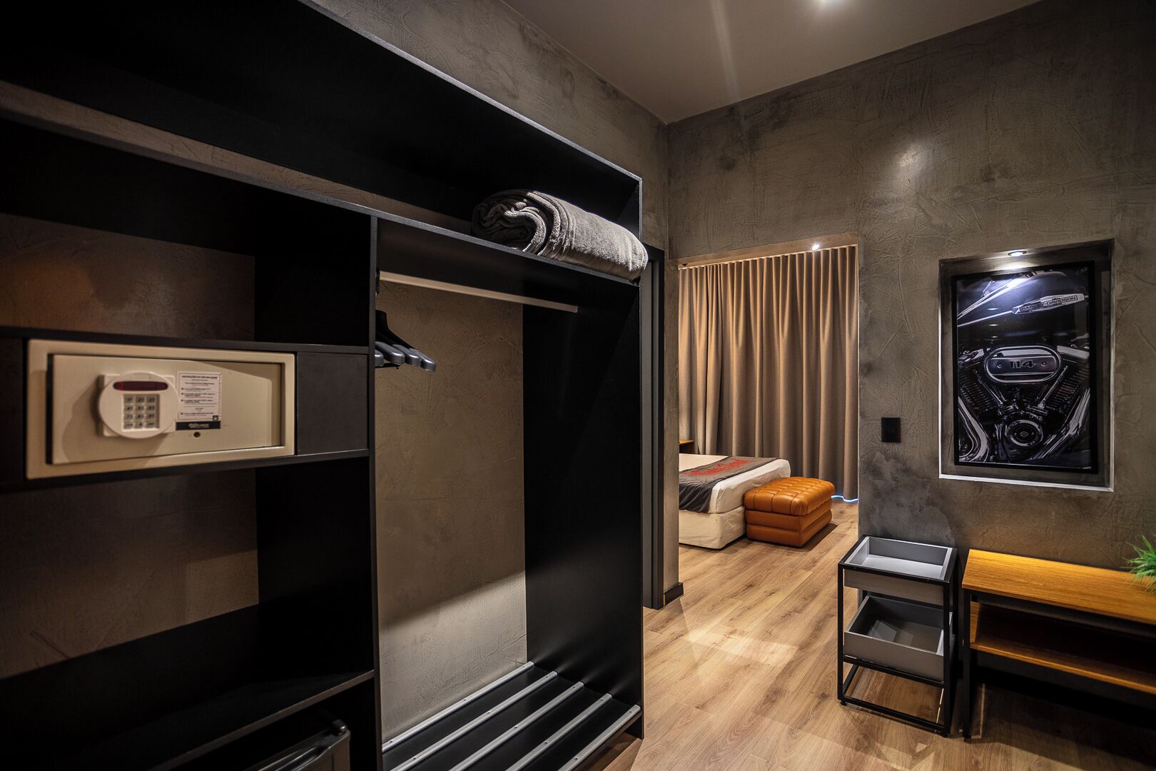 A modern hotel room with a wardrobe, a bed, a bench, and a framed picture on the wall.