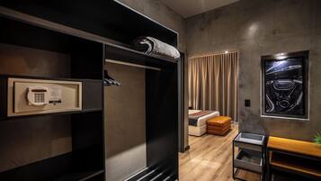 A modern hotel room with a wardrobe, a bed, a bench, and a framed picture on the wall.