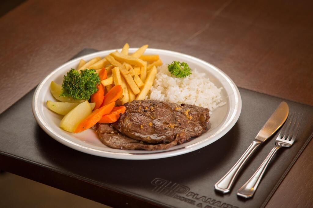 A plate with steak, fries, rice, and vegetables on a table.