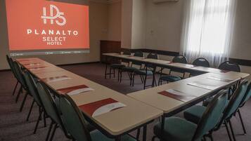 Un salón de conferencias en el Hotel Planalto Select con una mesa larga, sillas y una pantalla de proyección que muestra el logo del hotel.