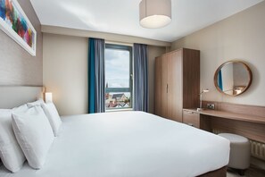 A hotel room with a large bed, a wooden wardrobe, a round mirror, and a view of the outside. - Cordia Serviced Apartments (Belfast)