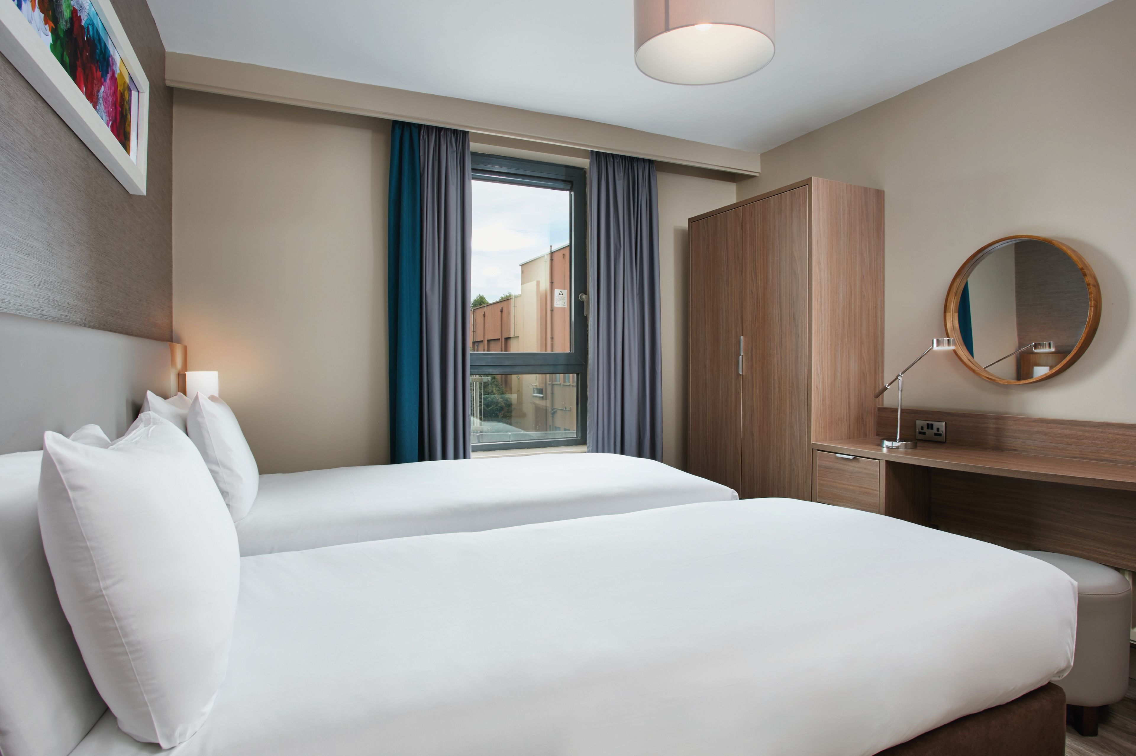 Habitación de hotel con dos camas, un armario de madera, un escritorio con espejo y una ventana con cortinas.