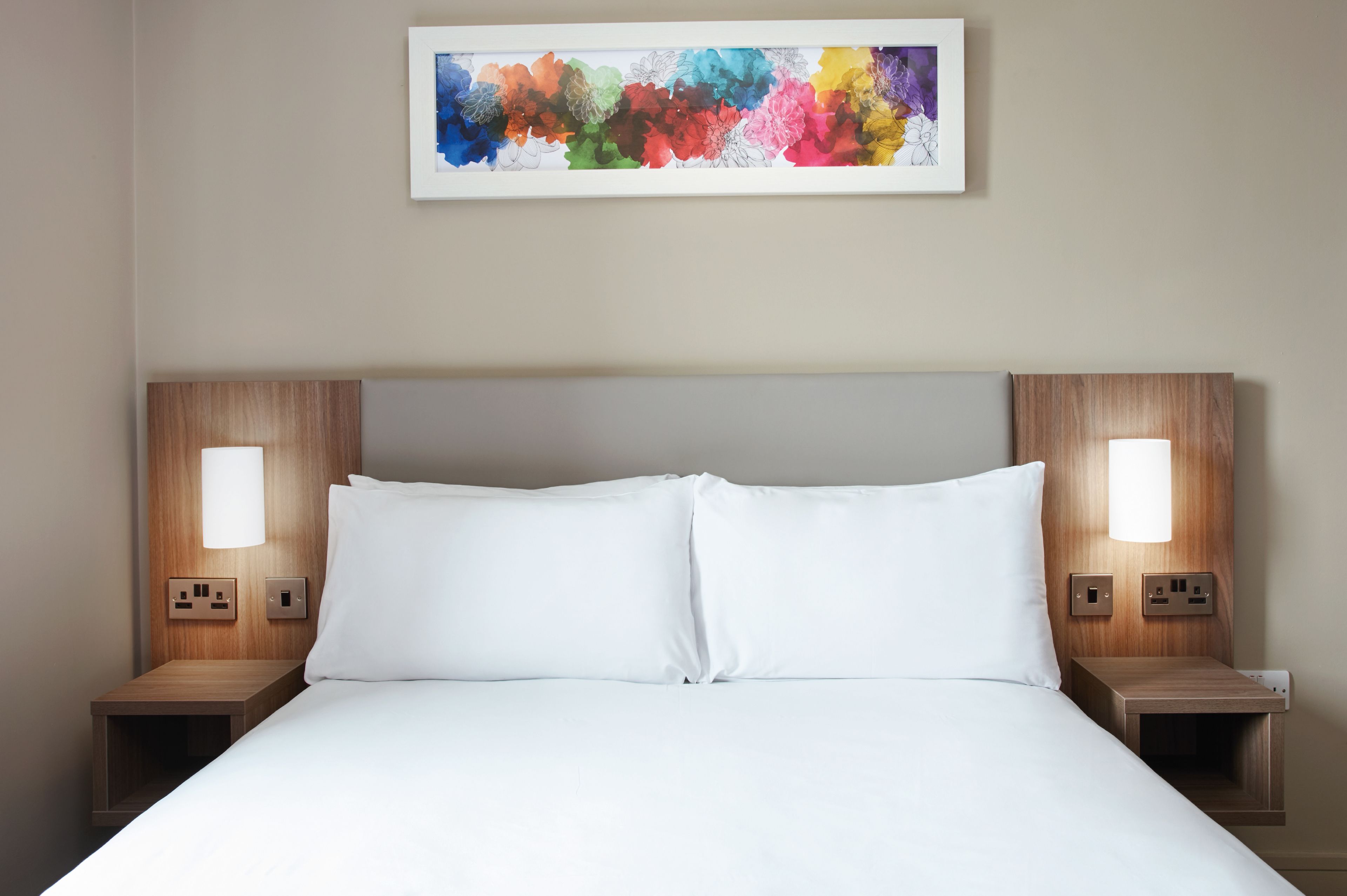 A neatly made bed with white linens, flanked by two bedside tables with integrated lamps and power outlets.