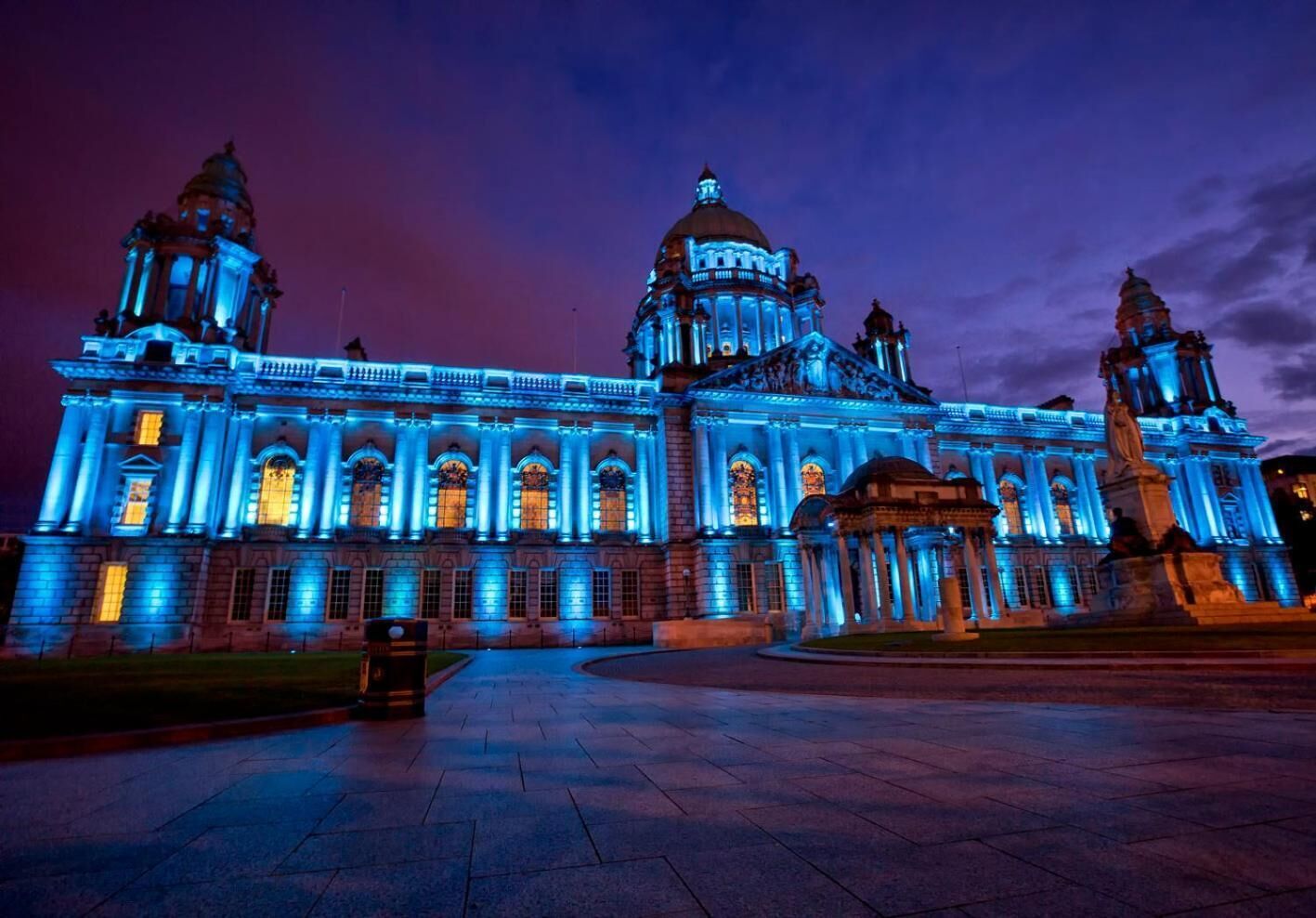 Un edificio grande e histórico con arquitectura clásica, que presenta columnas destacadas y una cúpula central, iluminado con luces azules.