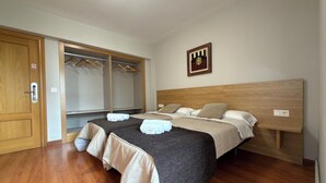 A hotel room with two beds, a wooden headboard, a wardrobe with hanging space, and a wall-mounted artwork. - The Hostal Iruñako (Burgos)
