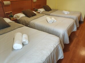 Habitación de hotel con tres camas individuales, cada una con una toalla enrollada y una almohada marrón.