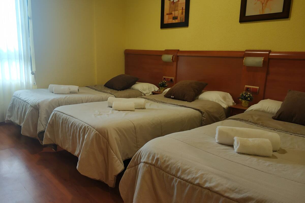A hotel room with three single beds, each with a neatly made bedspread and pillows.