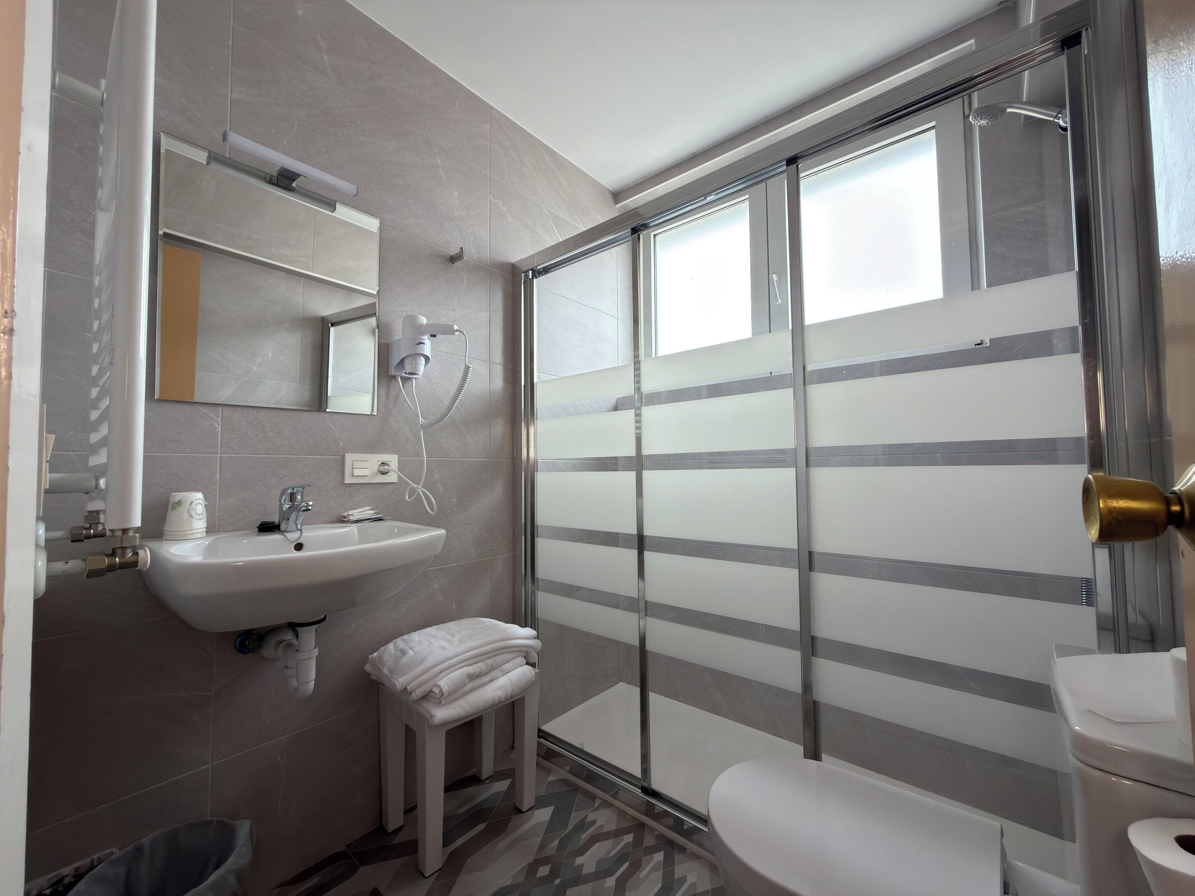 Un baño moderno con lavamanos, espejo, toallero y zona de ducha con puertas de vidrio esmerilado.