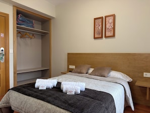 Habitación de hotel con una cama, un armario y dos cuadros en la pared.