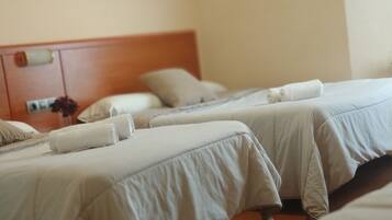 Three comfortable beds with white bedspreads and towels, set against a light-colored backdrop.