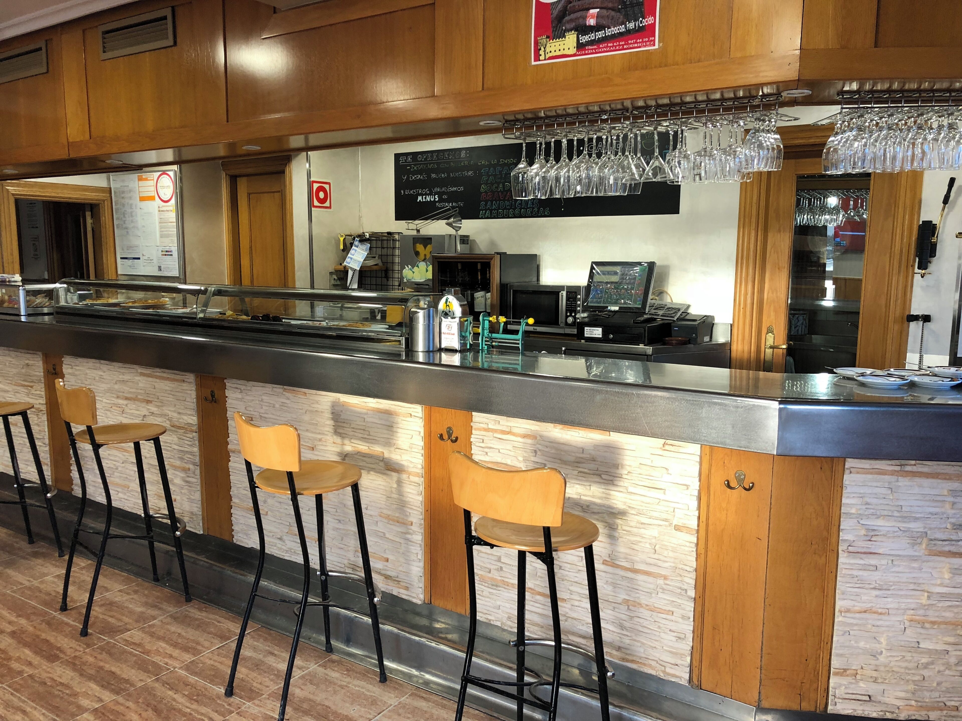 Zona de bar con taburetes, mostrador, panel con la carta y caja registradora.
