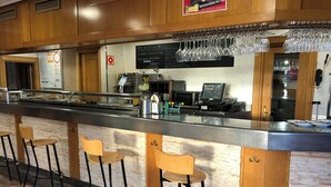 A bar area with stools, a counter, a menu board, and a cash register. - The Hostal Iruñako (Burgos)