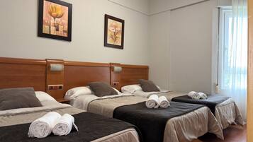 Habitación de hotel con tres camas, cada una con una almohada y toallas enrolladas. Encima de las camas, hay dos cuadros enmarcados en la pared.