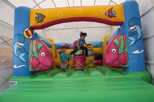 Un área de juegos inflable colorida con diseños de peces de dibujos animados y un niño jugando.