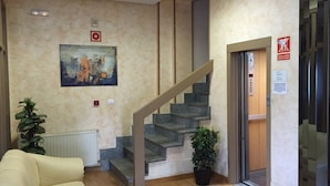 A hotel lobby with a staircase, a painting, a sofa, and a potted plant. - The Hostal Iruñako (Burgos)