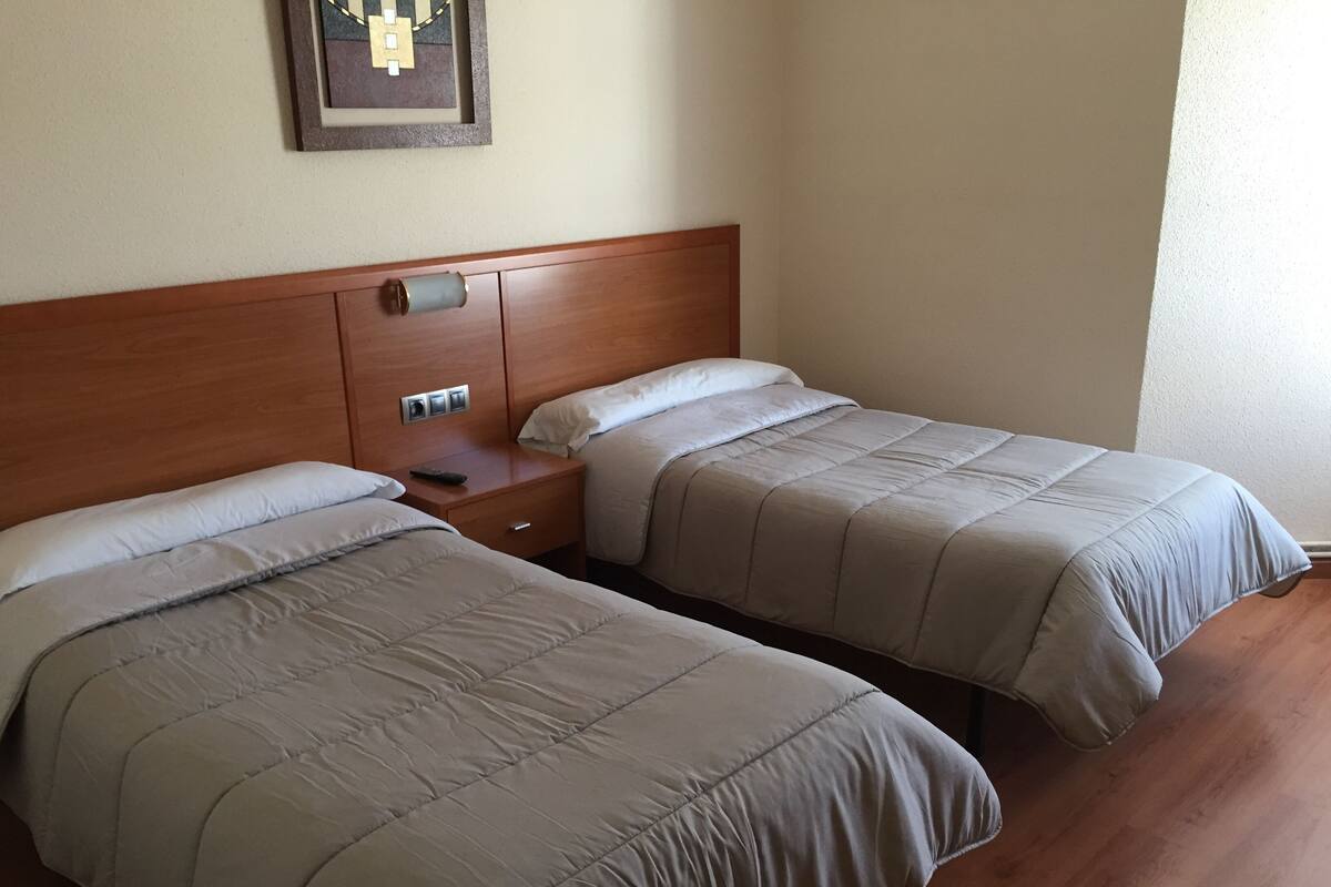 A hotel room with two beds, wooden headboards, a nightstand with a remote control, and a framed picture on the wall.