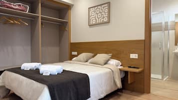 Una habitación de hotel con cama, armario, mesita de noche y zona de ducha.