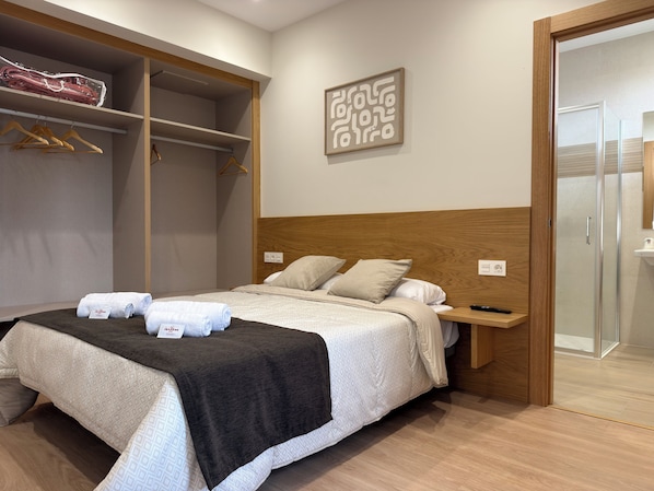 A hotel room with a bed, a wardrobe, a bedside table, and a shower area.