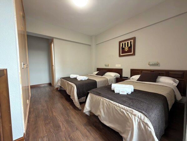 A hotel room with two beds, wooden flooring, a painting on the wall, and a door leading to another room.
