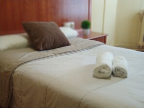 Una cama bien hecha con una almohada marrón y dos toallas enrolladas.