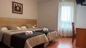 A hotel room with two beds, a wooden headboard, a desk, a chair, a television, and a window with curtains.