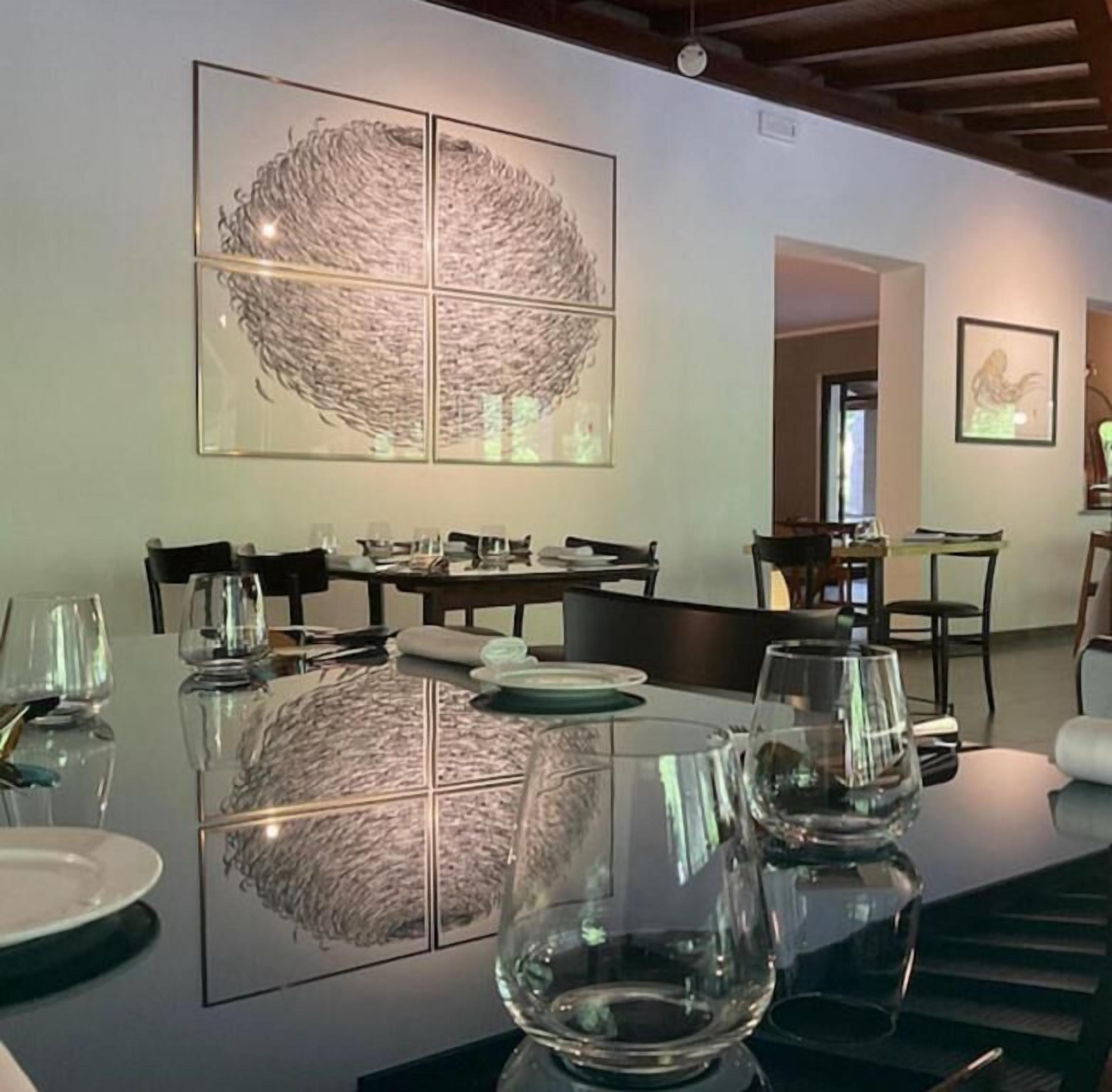 Un espace repas avec une grande table dressée pour le repas, un plafond avec des poutres apparentes et des œuvres d’art encadrées accrochées aux murs.