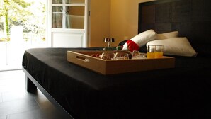 Habitación de hotel con cama, una bandeja con cosas para el desayuno, ventana con cortinas y vistas a árboles.