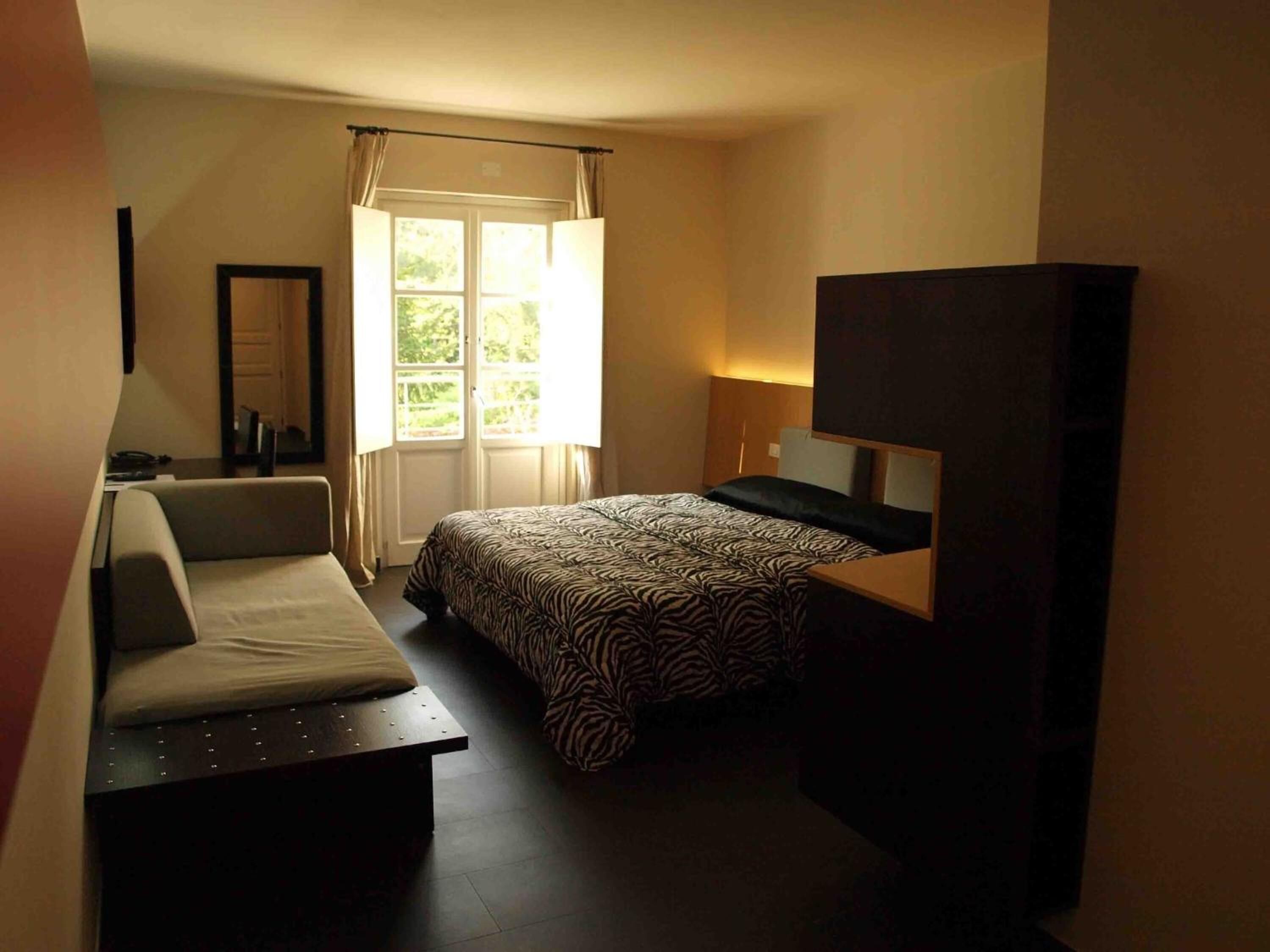A bedroom with a bed, a desk, a chair, a TV, and a window with curtains.