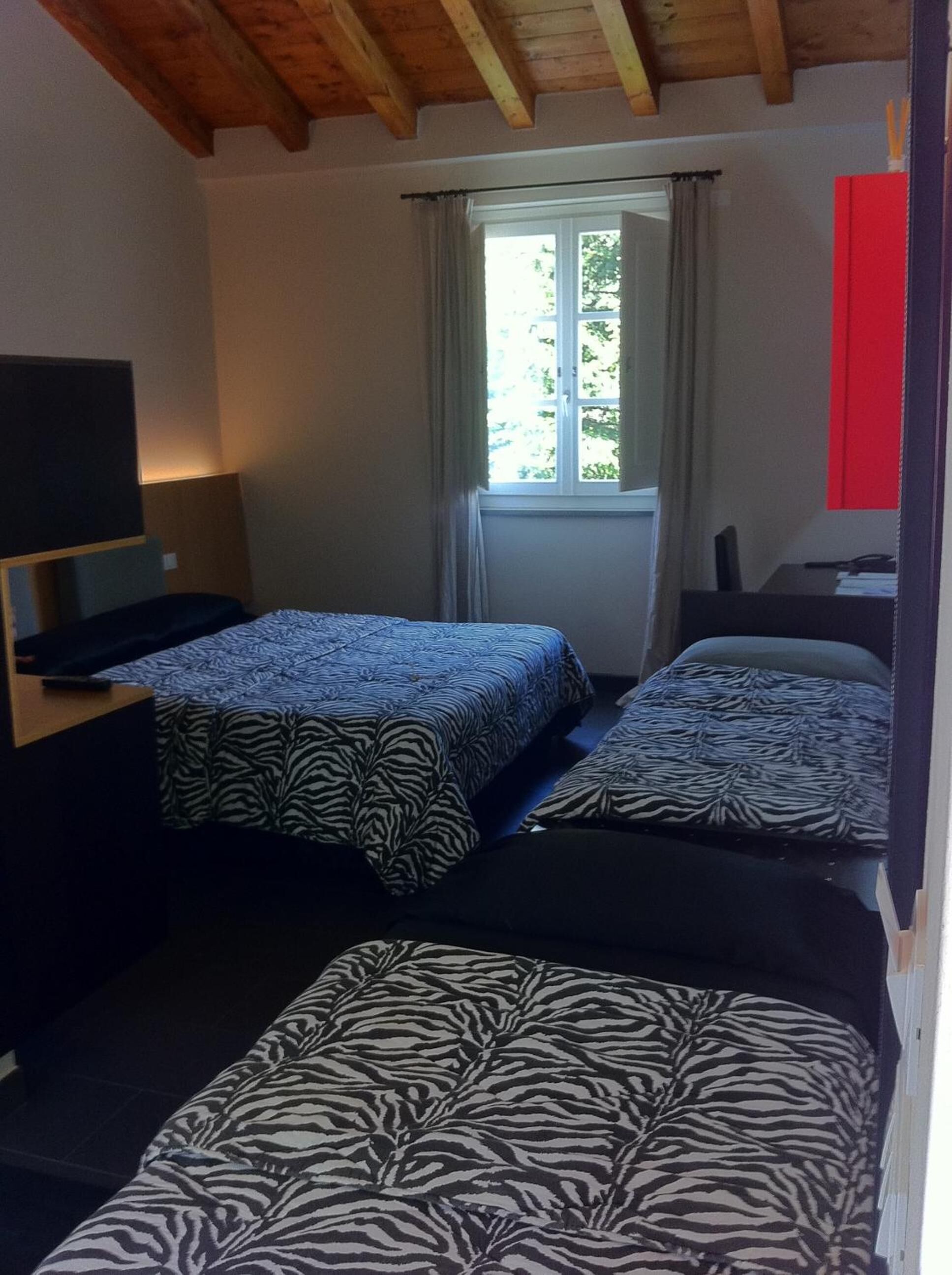 Une chambre avec deux lits, un bureau avec un ordinateur, une fenêtre avec des rideaux et un mur rouge.