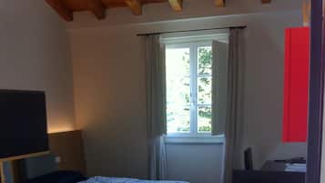 A room with two beds, a desk with a computer, a window with curtains, and a red wall.