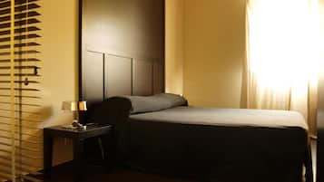 Ein Hotelzimmer mit Bett, Nachttisch mit Lampe und Fenster mit Vorhängen.