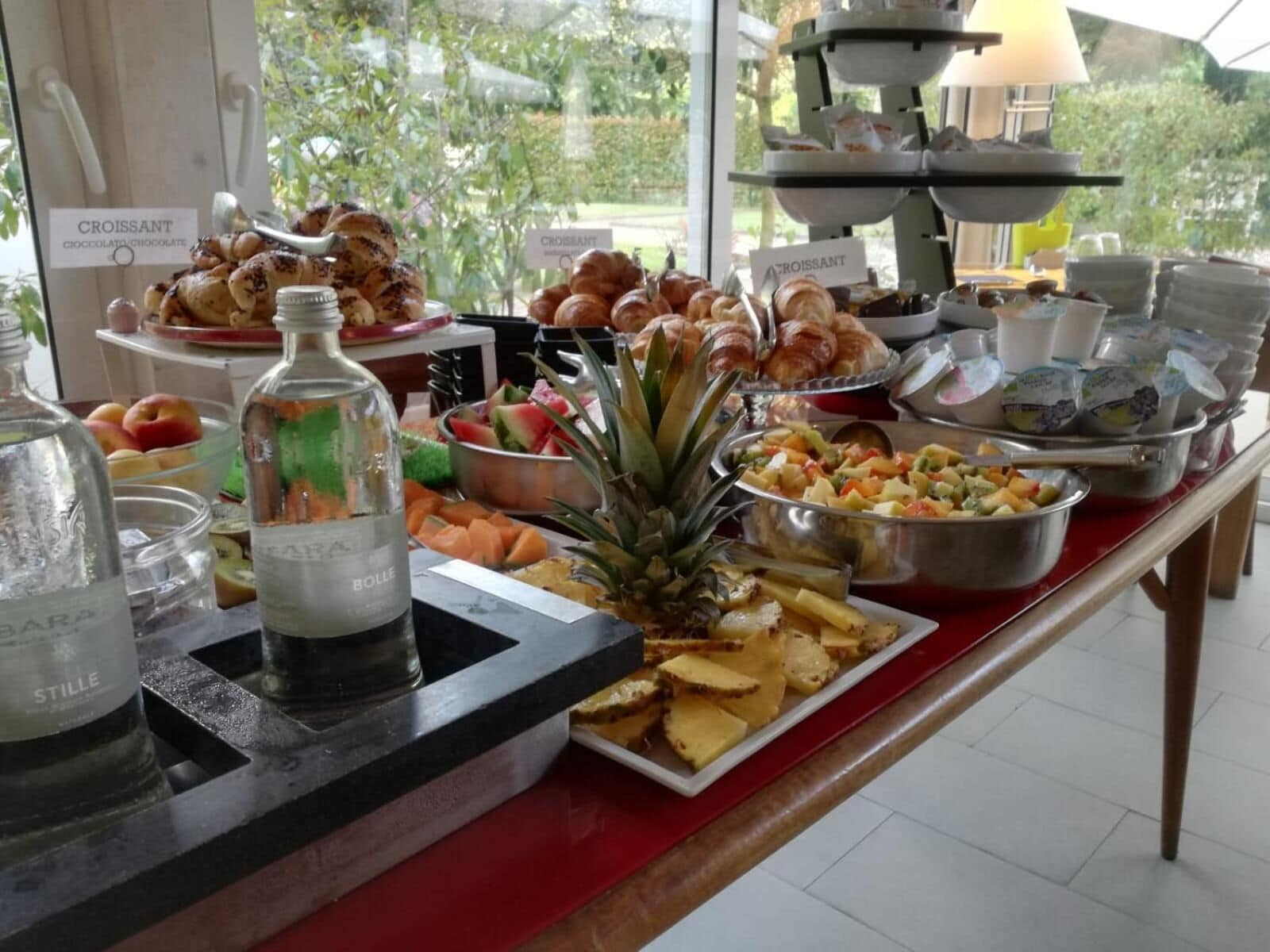 A buffet with croissants, fruits, and a bottle of BOLLE water.