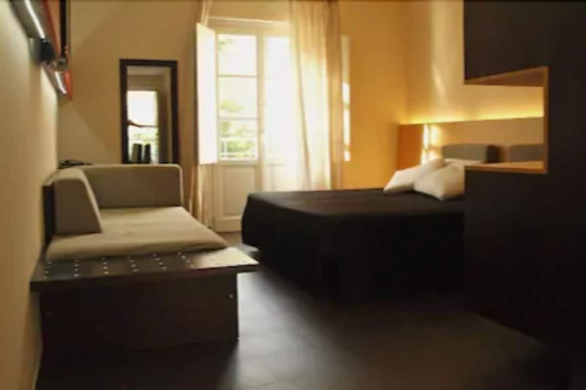 A narrow hotel corridor with a bed, a sofa, and a small table.