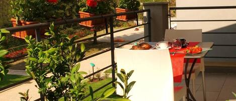 Un patio al aire libre con una mesa lista para comer, rodeado de plantas y flores en macetas.