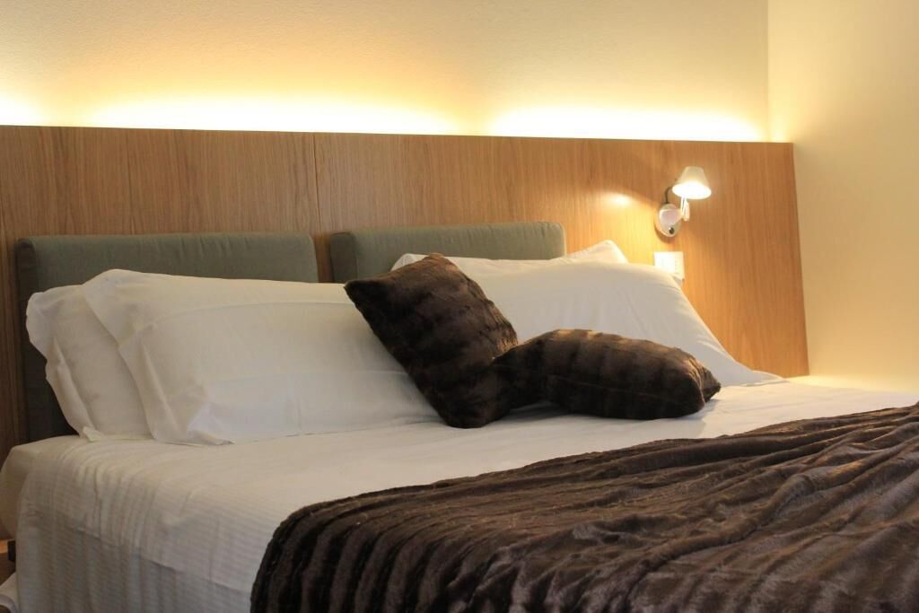Une chambre d’hôtel avec un lit, des oreillers, une couverture et un luminaire fixé au mur.
