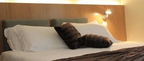 Una habitación de hotel con cama, almohadas, una colcha y una lámpara de pared.